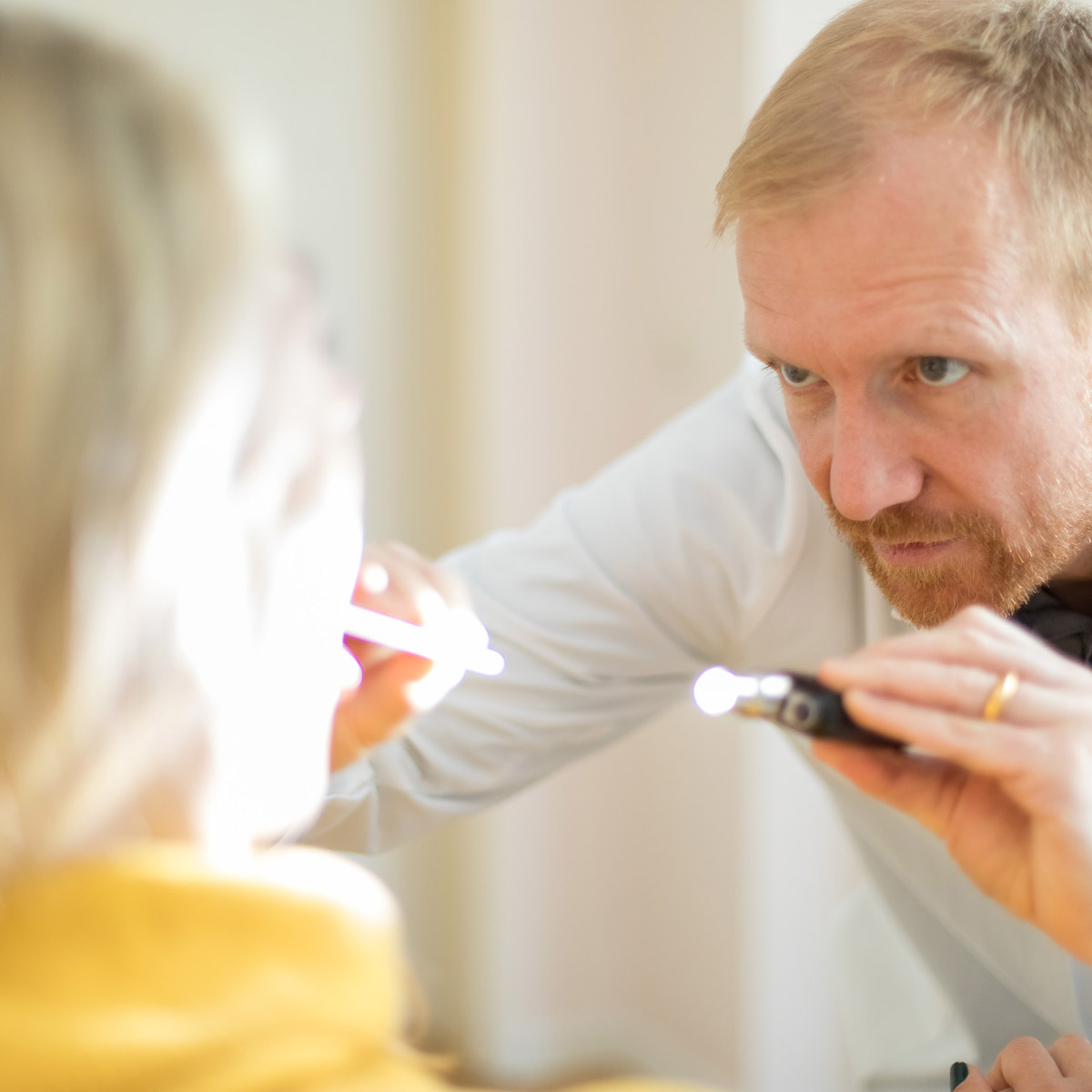 HNO-Arzt untersucht das Ohr einer Patientin mit einem medizinischen Untersuchungsinstrument in der Praxis.